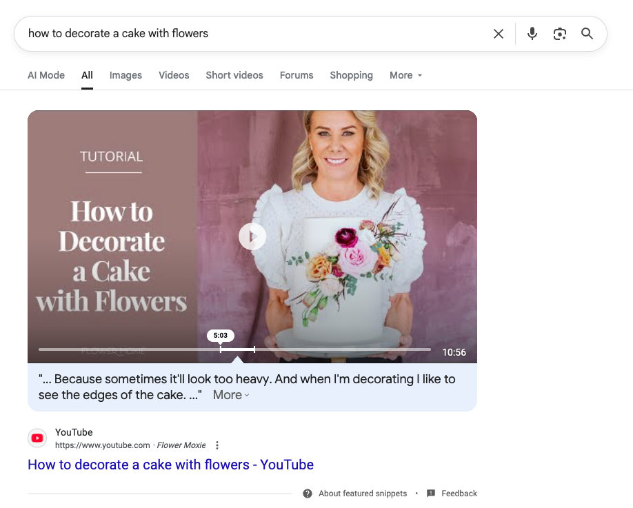 Featured video result for "how to decorate a cake with flowers" showing tutorial and woman holding decorated cake.